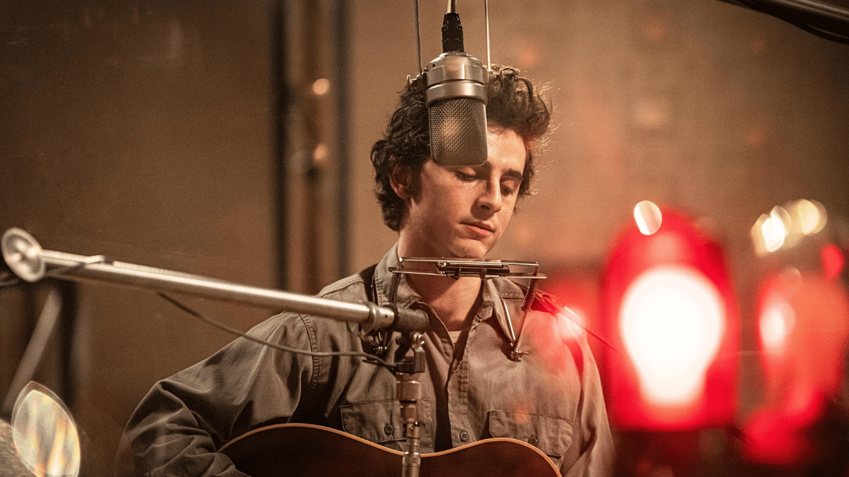 Singer playing acoustic guitar in recording studio while singing into a microphone