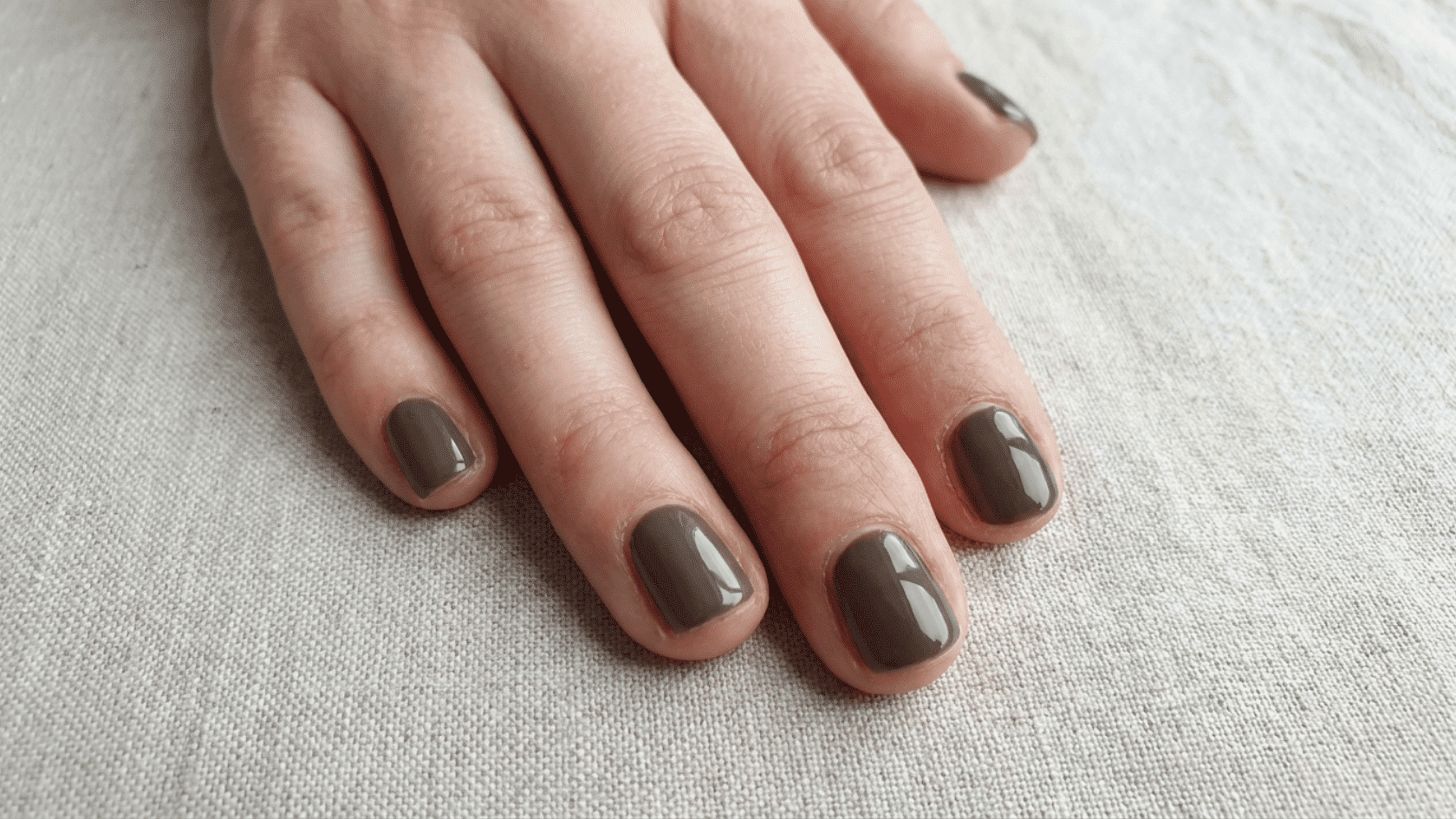 Close-up view of short nails with glossy dark gray gel polish on a hand.