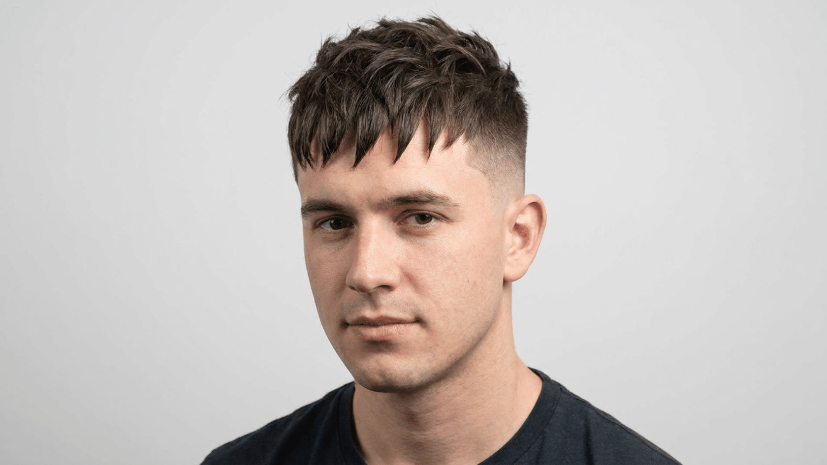 Textured fringe hairstyle for men with thinning hair showing choppy irregular fringe with separated pieces and tight fade on sides, front view.