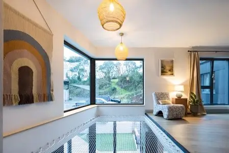 Modern living room with large windows, wall tapestry, and cozy seating under warm lighting.
