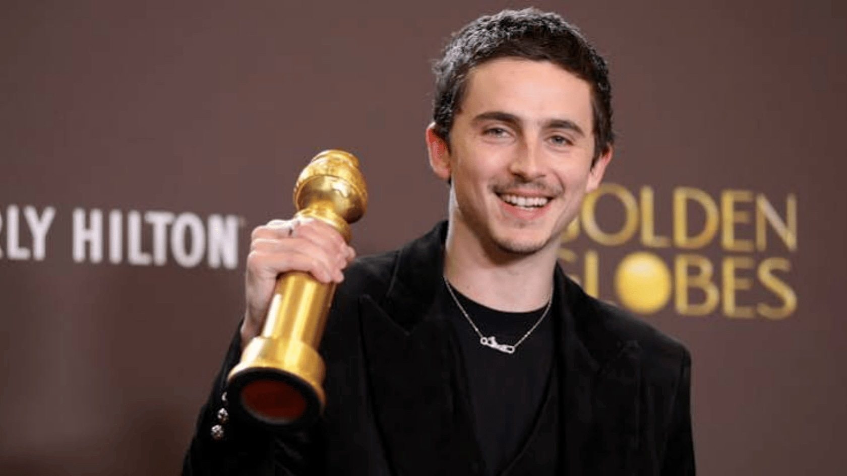 Timothee Chalamet holding a golden award trophy while smiling at an awards event.