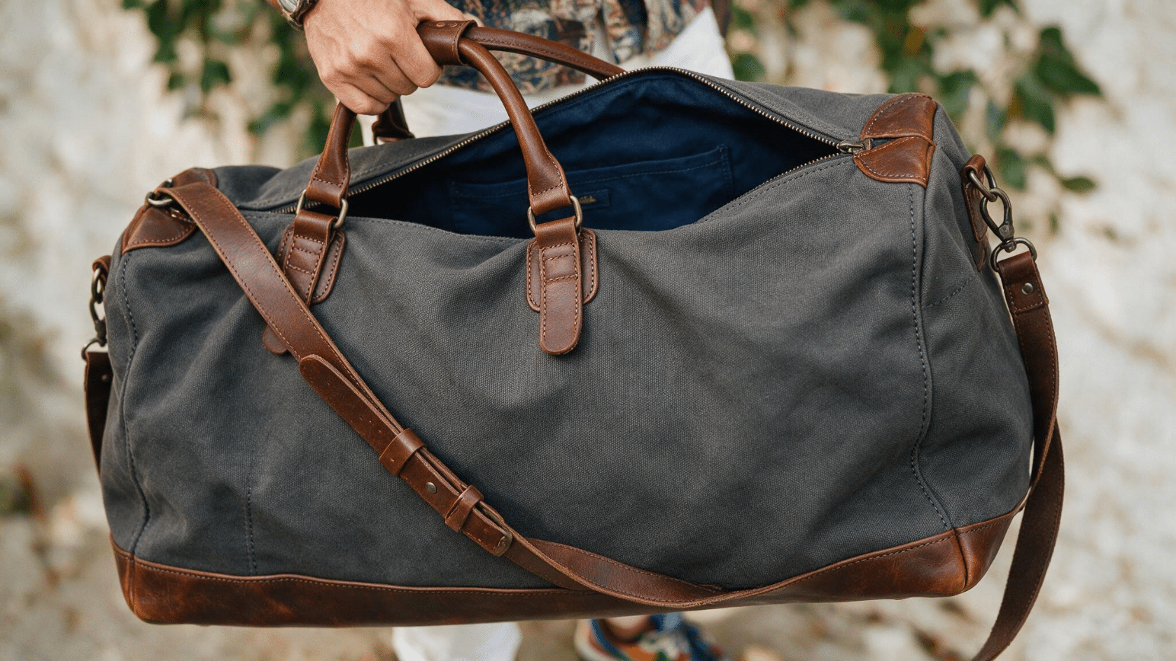 Traveler holding an open gray duffel bag with brown leather handles and shoulder strap.