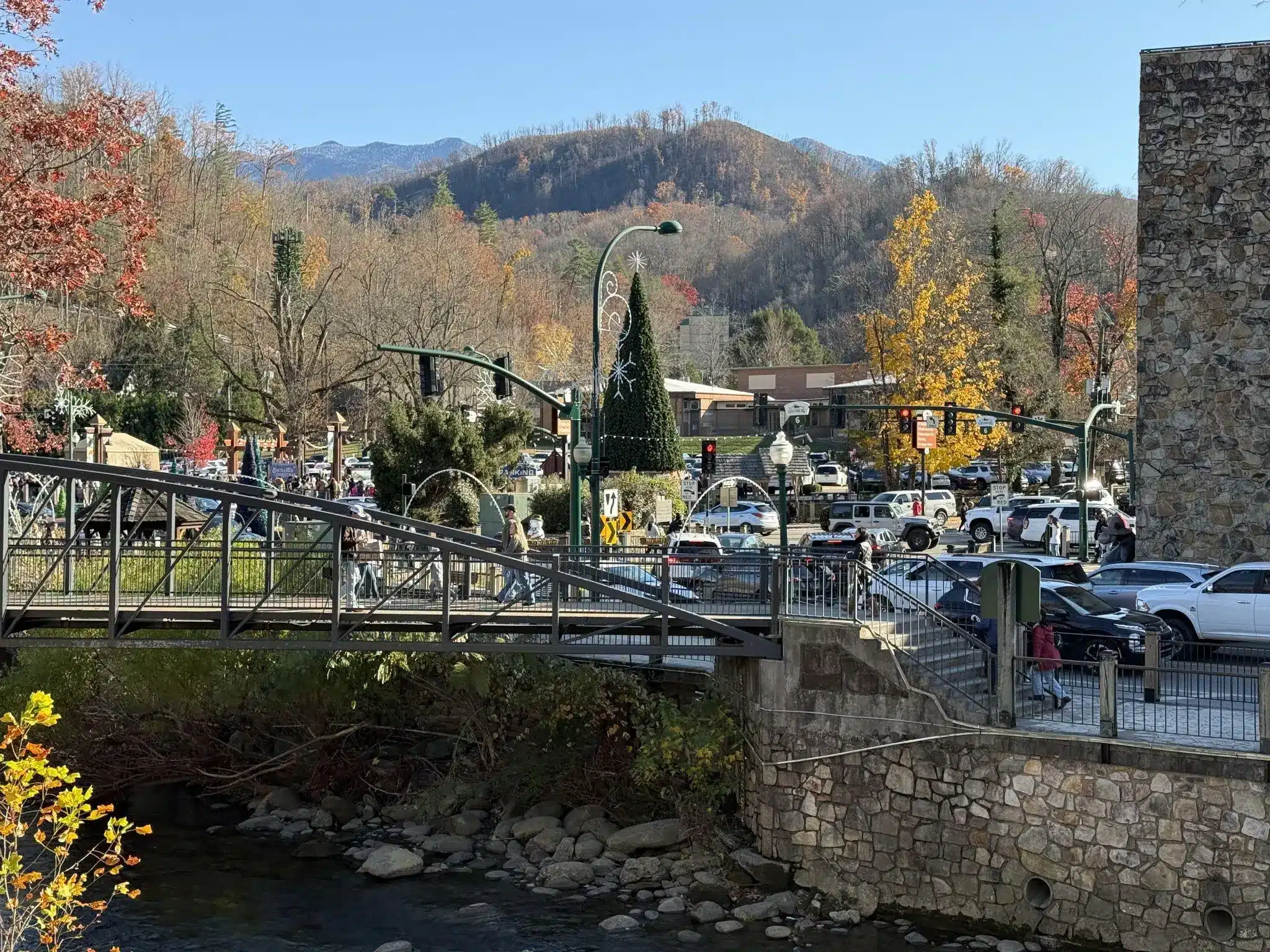 Pedestrian bridge over creek with autumn trees and parked cars in a small mountain town