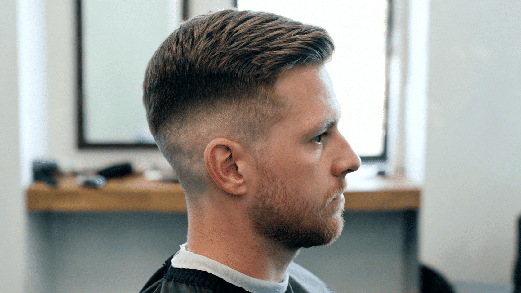 Man with a classic undercut haircut and neatly styled top shown in side profile in a barbershop.