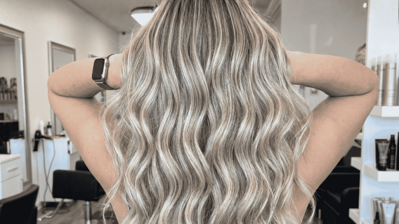 Long wavy hair with full blonde highlights distributed evenly throughout all layers, photographed from the back in a salon setting.