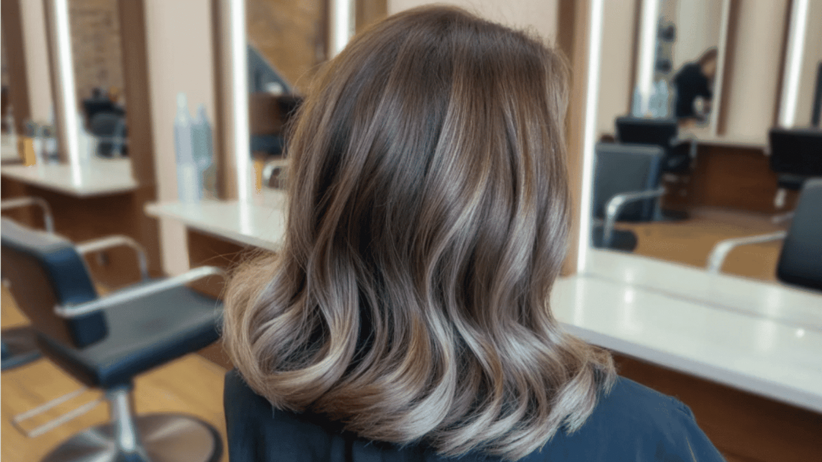Medium-length brunette hair with soft ash blonde <echighlighted>partial highlights</echighlighted> concentrated on the ends and top layers, photographed in a salon setting.