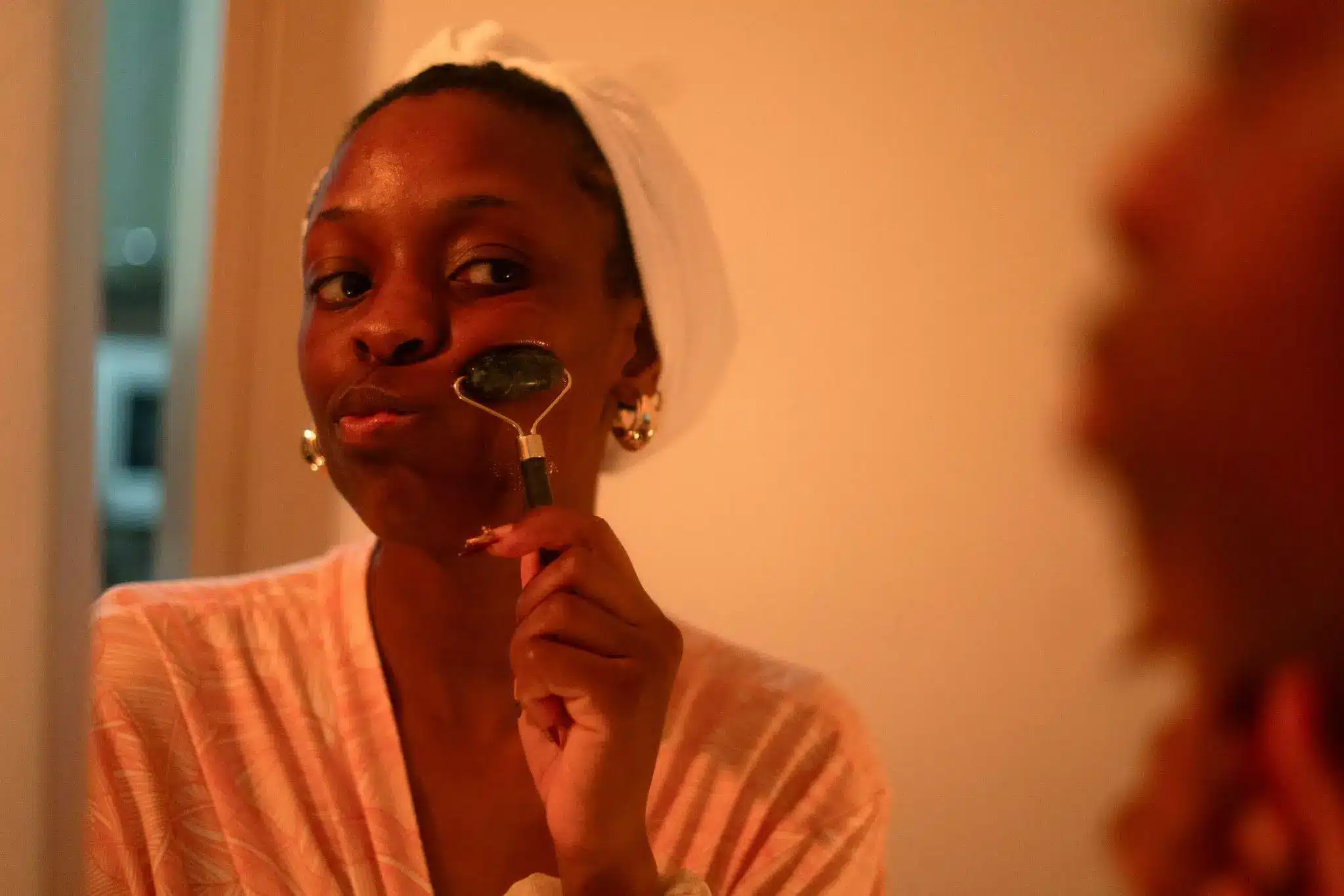 Person using jade roller on face in dimly lit bathroom setting