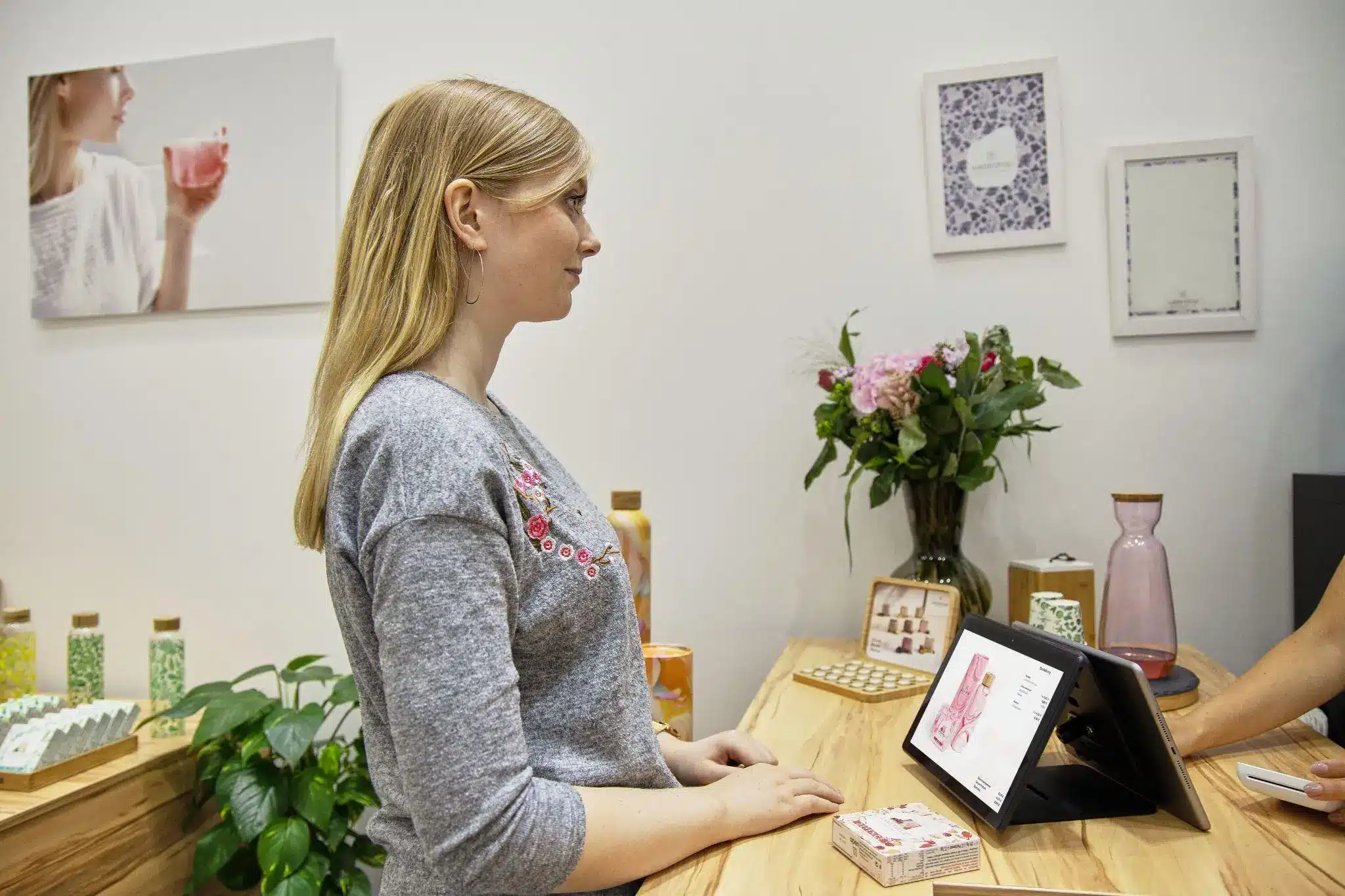 Woman at wooden counter completing transaction with tablet in bright, modern shop environment