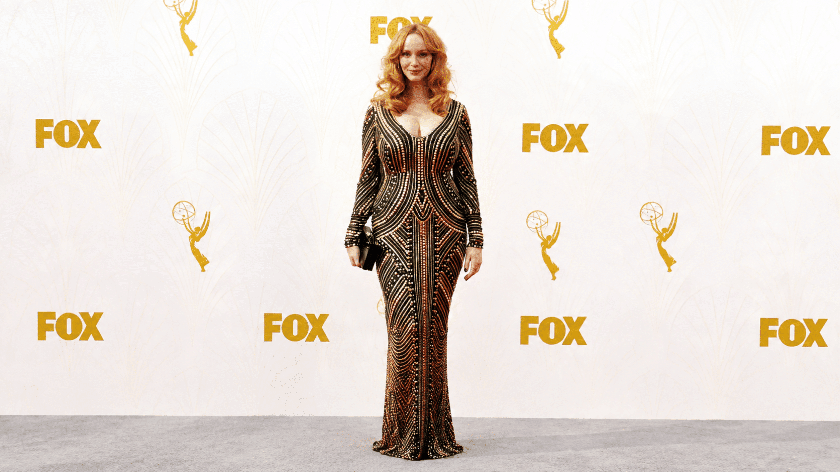 Woman wearing a black and gold embellished gown on a red carpet with an awards backdrop.