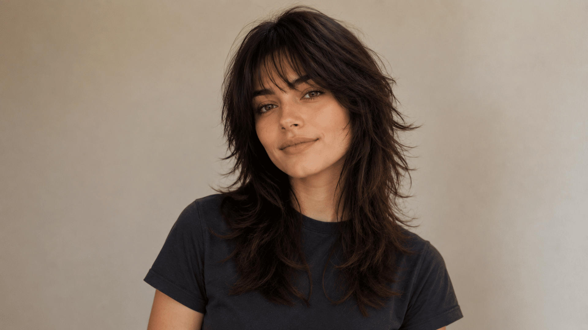 Woman with dark layered wolf cut and wispy bangs against a neutral background.