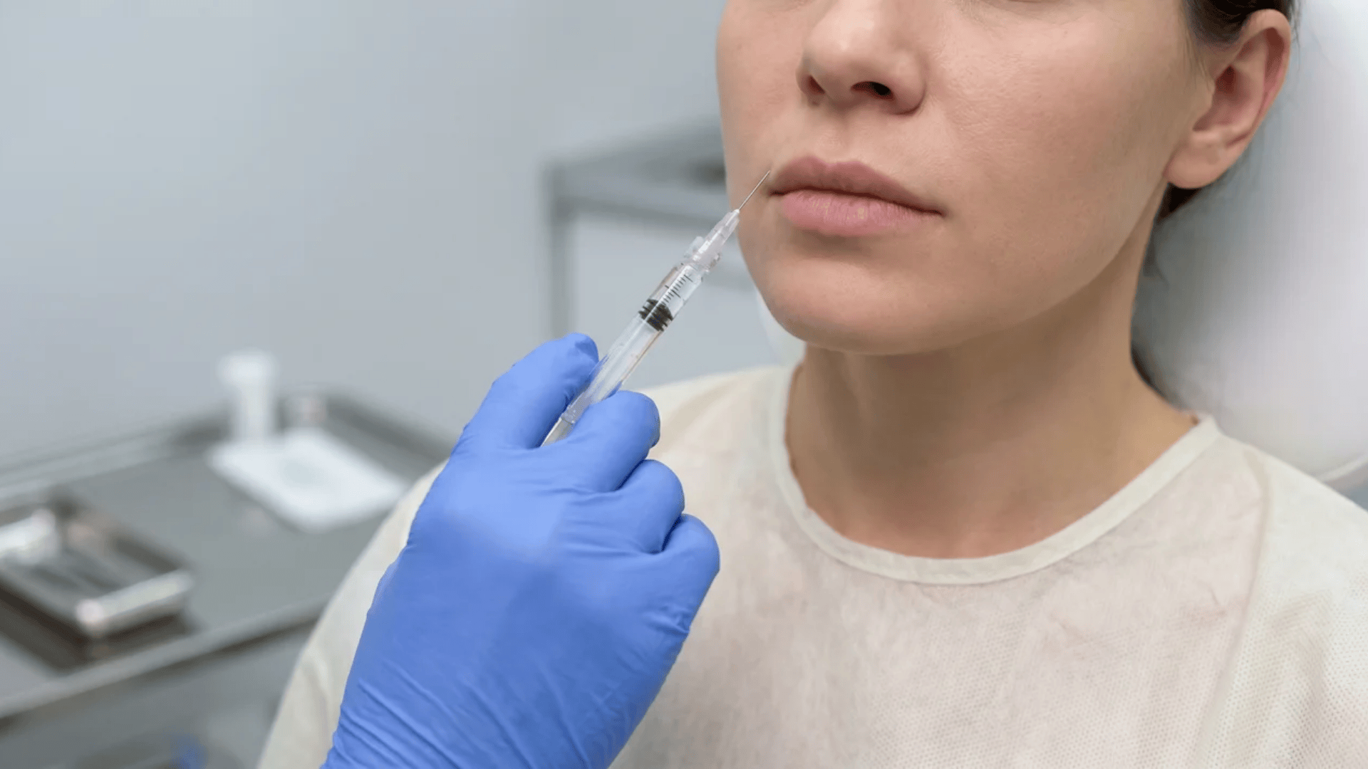 A practitioner uses a syringe to perform a cosmetic lip injection on a woman's upper lip in clinic.