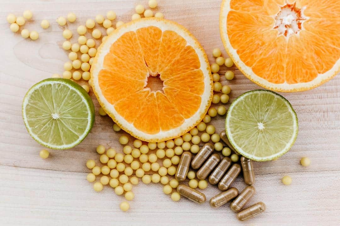 Sliced orange and lime on wooden surface with capsules and yellow tablets scattered