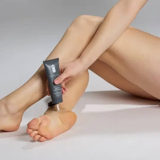 Person applying foot cream to heel in a neutral setting with soft lighting