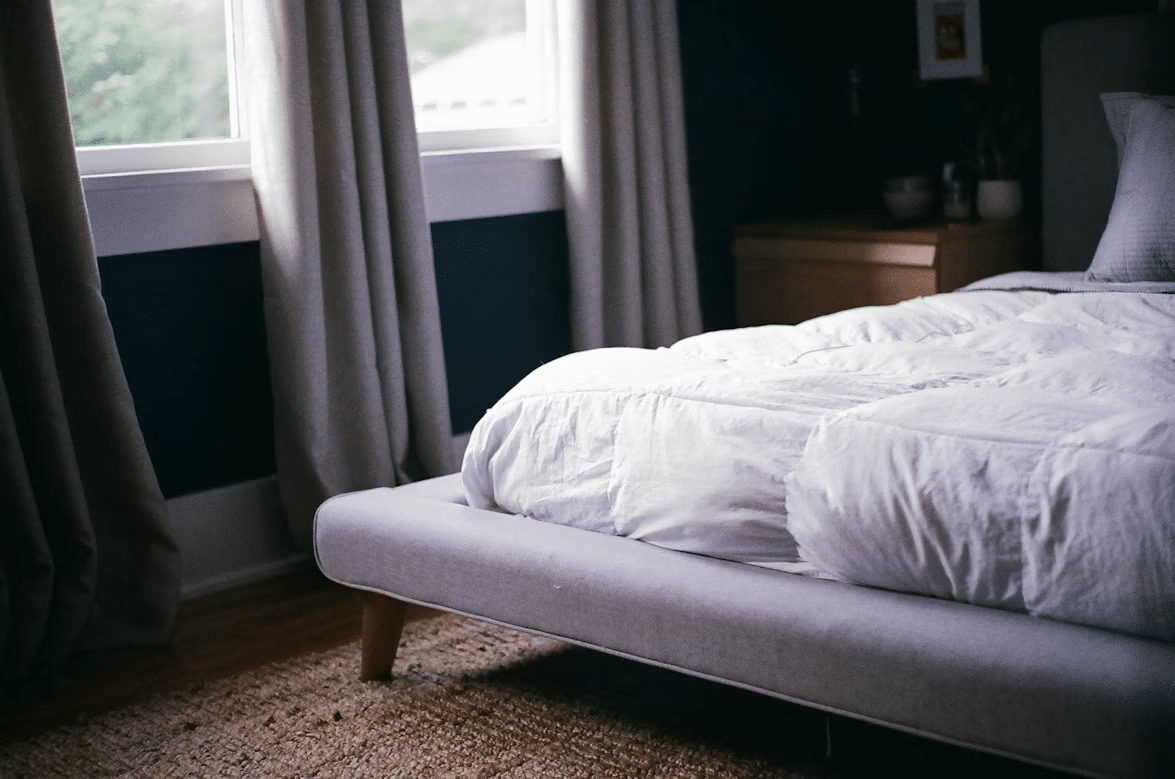 Cozy bedroom with white bedding on grey upholstered bed near large window with curtains