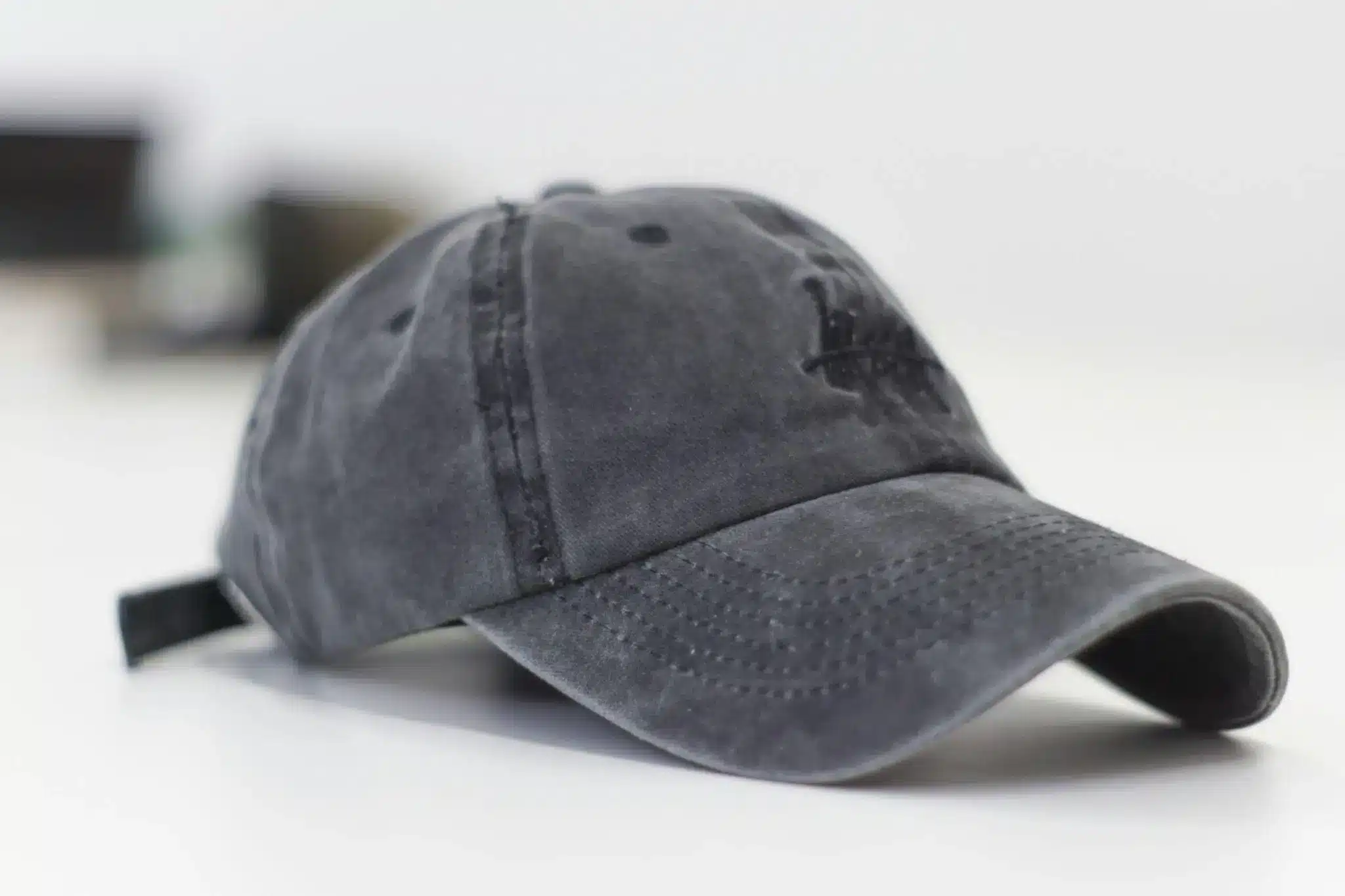 Gray baseball cap with embroidered logo on white surface in soft lighting