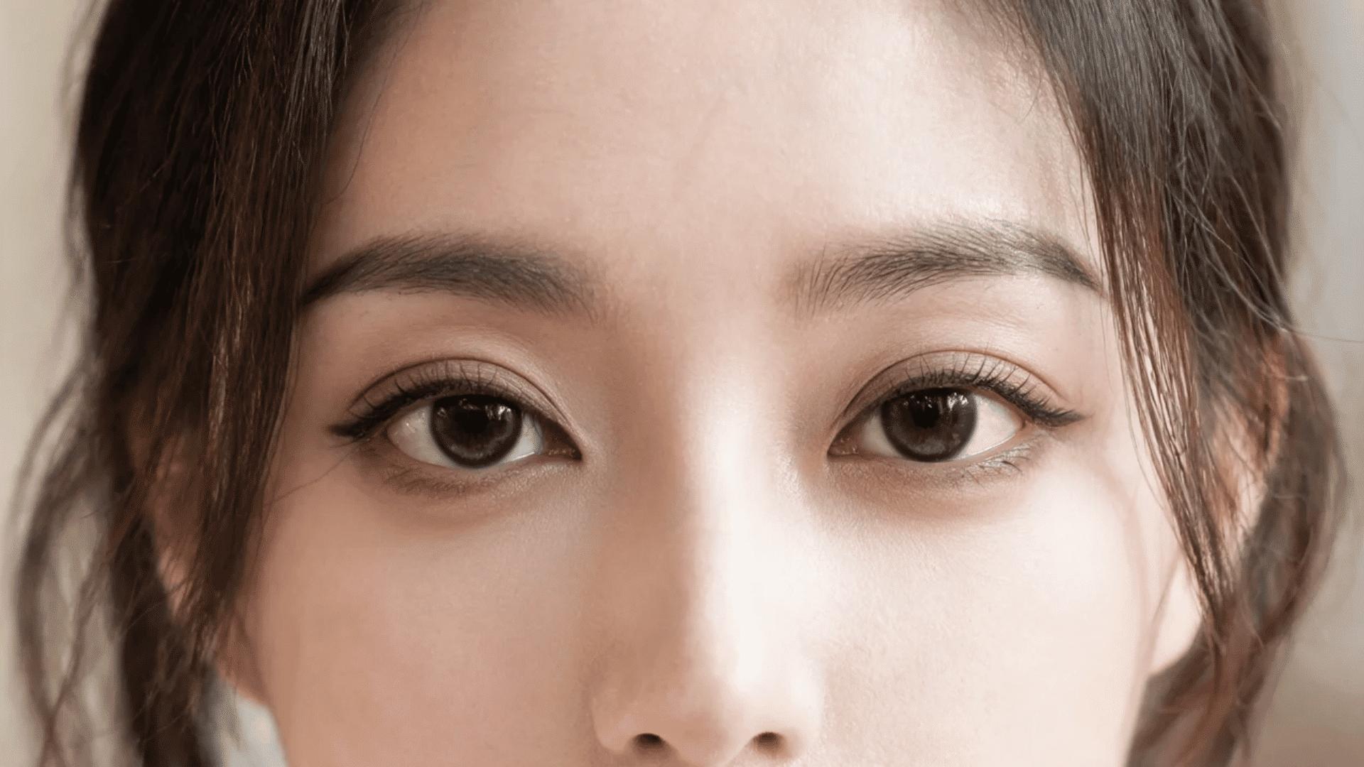 Close-up of a woman with dark eyebrows, brown eyes, lashes, and hair framing the face