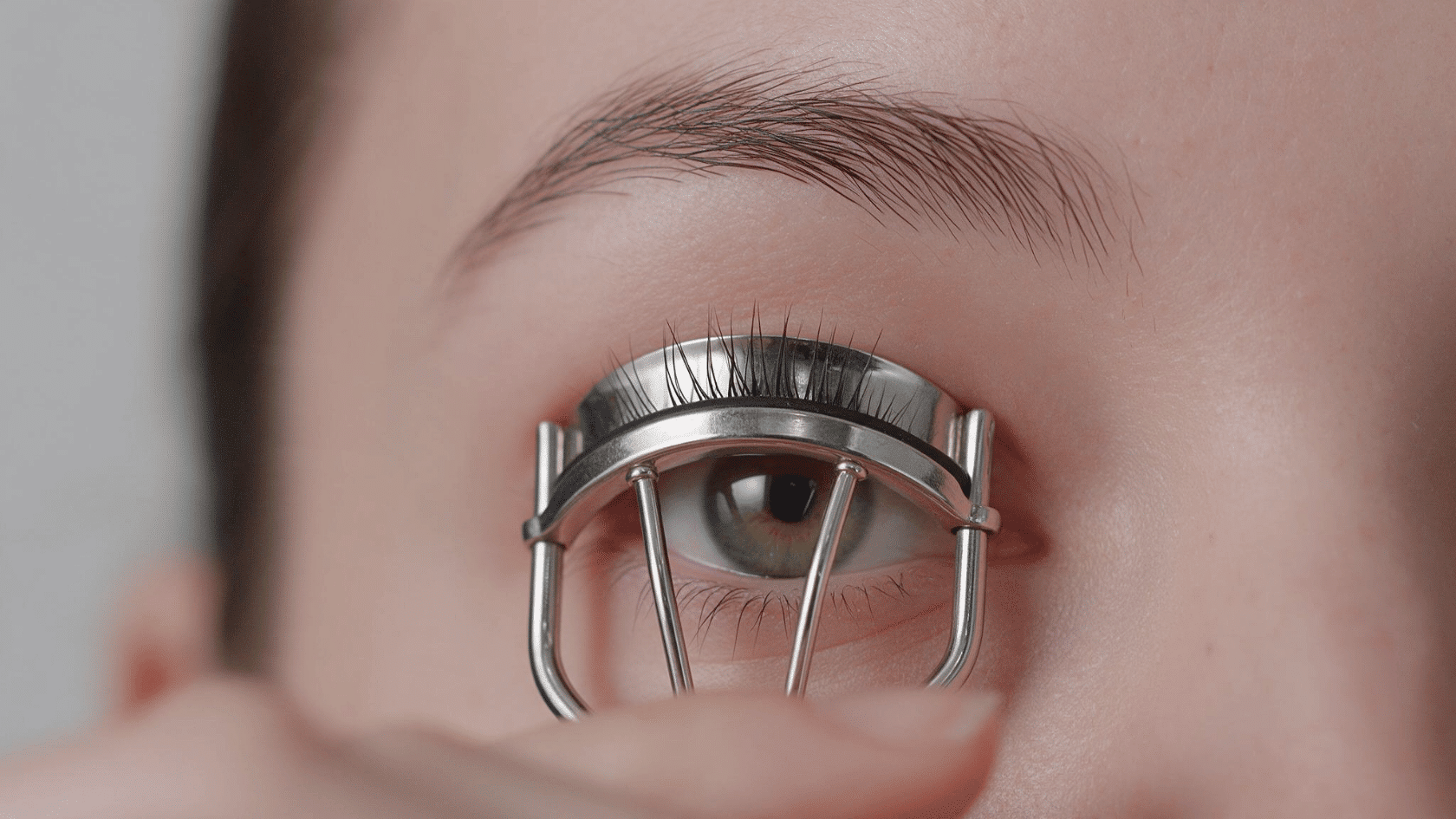 Close-up of a woman curling her upper eyelashes with a metal eyelash curler.