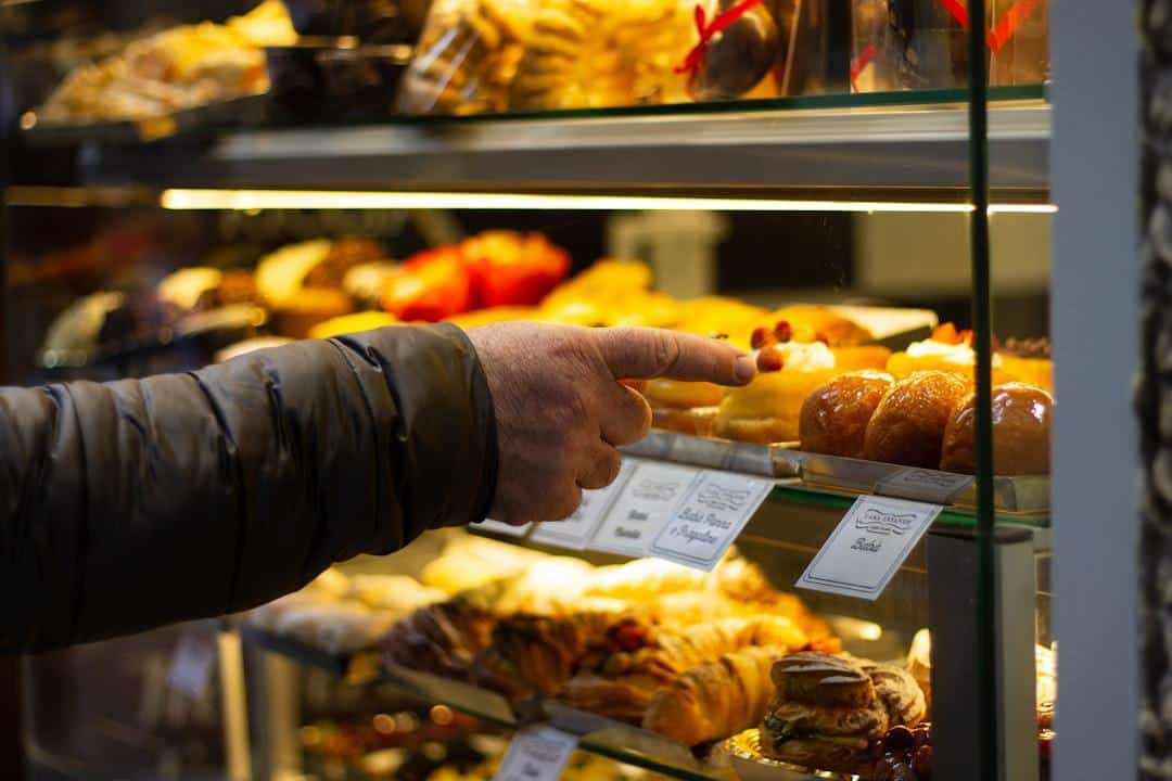 Hand pointing at pastries inside a glass display case in a bakery with warm lighting