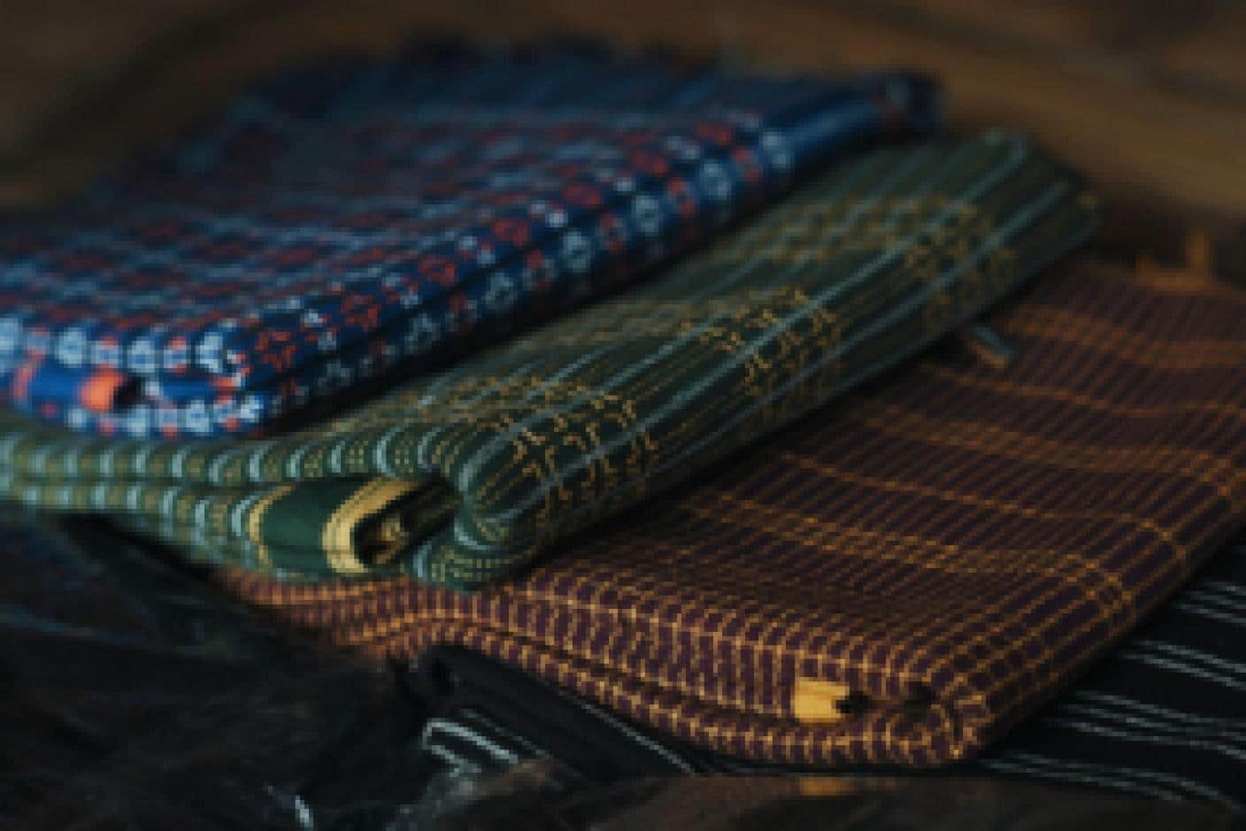 Folded colorful patterned fabrics stacked on a wooden surface in warm lighting