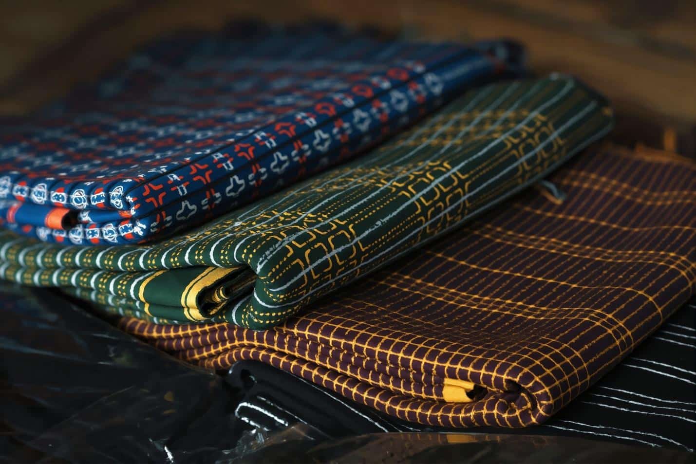 Stack of folded patterned fabrics in various colors and designs on dark surface