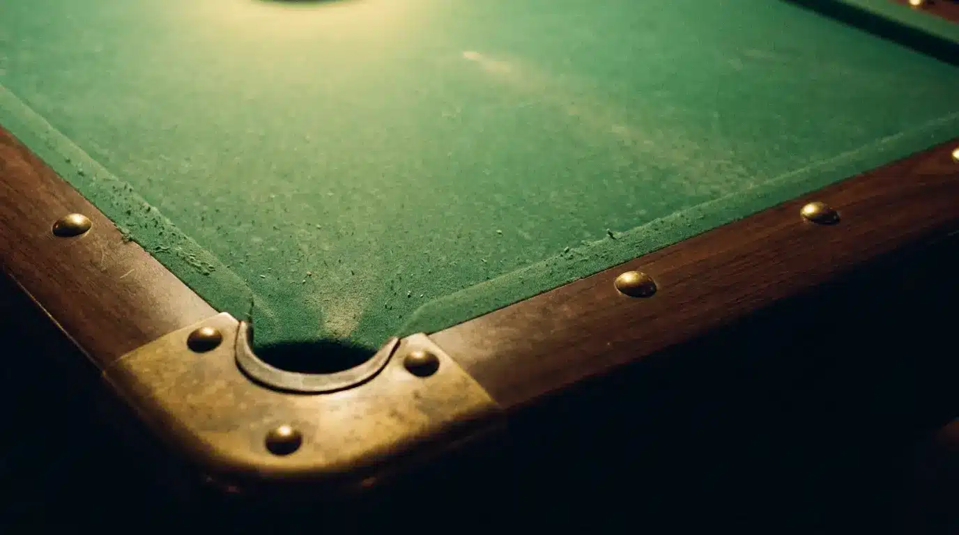 Close-up of corner pocket on vintage green pool table with brass rivets in dim lighting