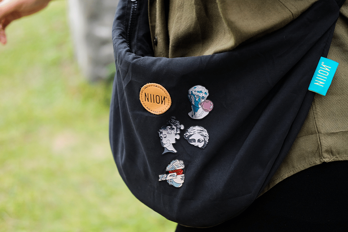 Black bag with artistic enamel pins and leather patch outdoors on a person wearing green jacket