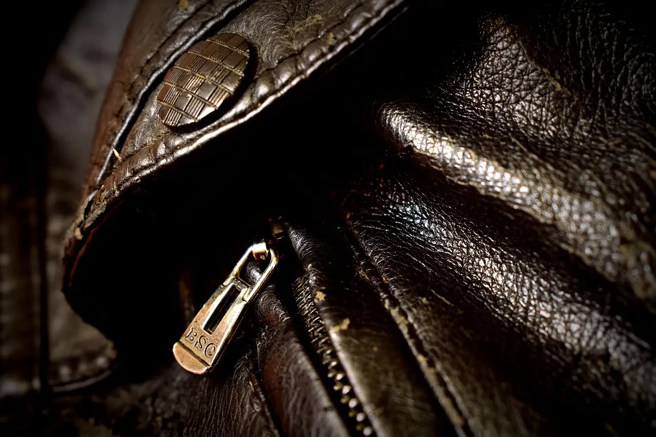 Close-up of a brown leather jacket with brass zipper and textured button