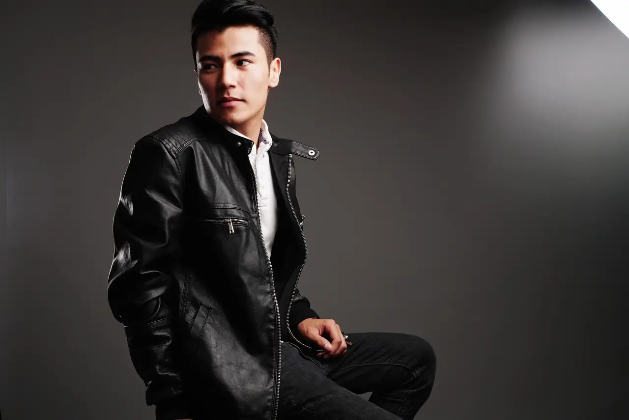 Man in black leather jacket posing against dark studio background