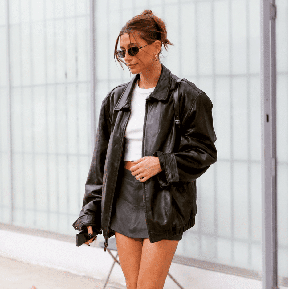 Hailey Bieber in an oversized black leather jacket and mini skirt, showcasing edgy retro fashion trends.