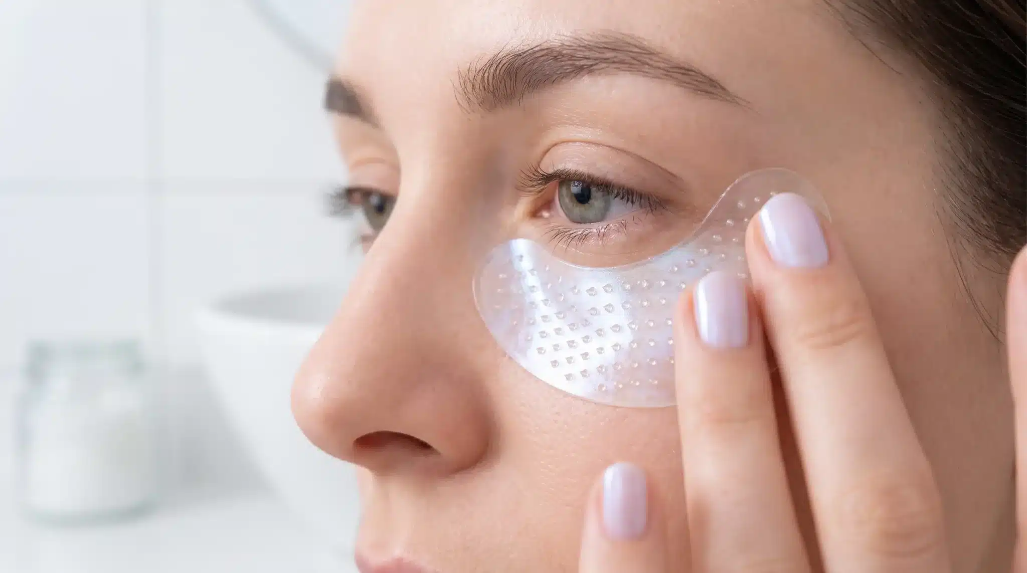 Under-eye mask applied to young woman's face close-up in bright bathroom setting