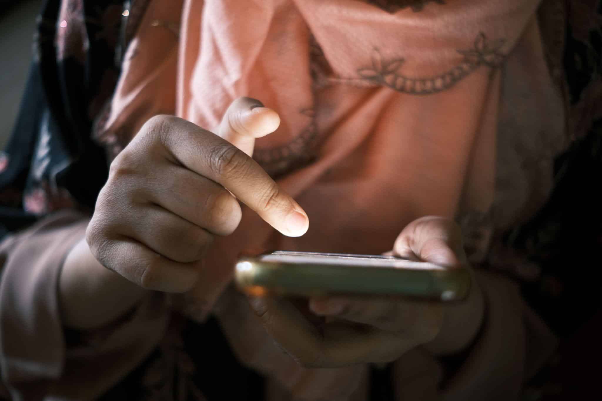 Hands using a smartphone in dim lighting with pink scarf visible