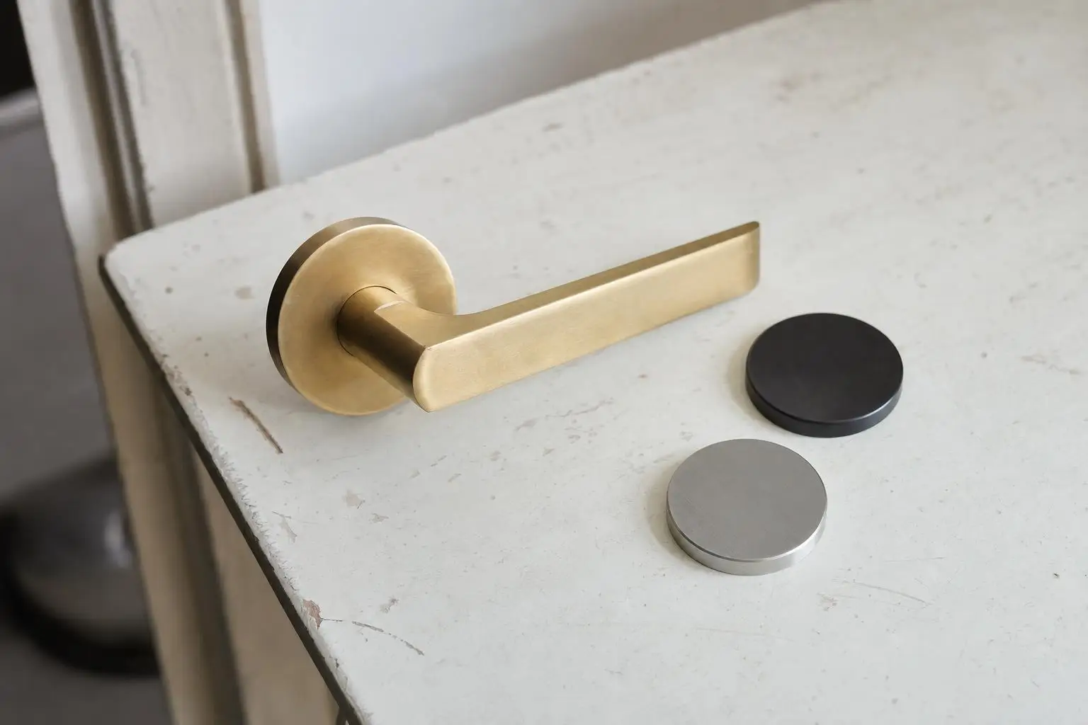 Gold door handle with two additional round color samples on white wooden surface