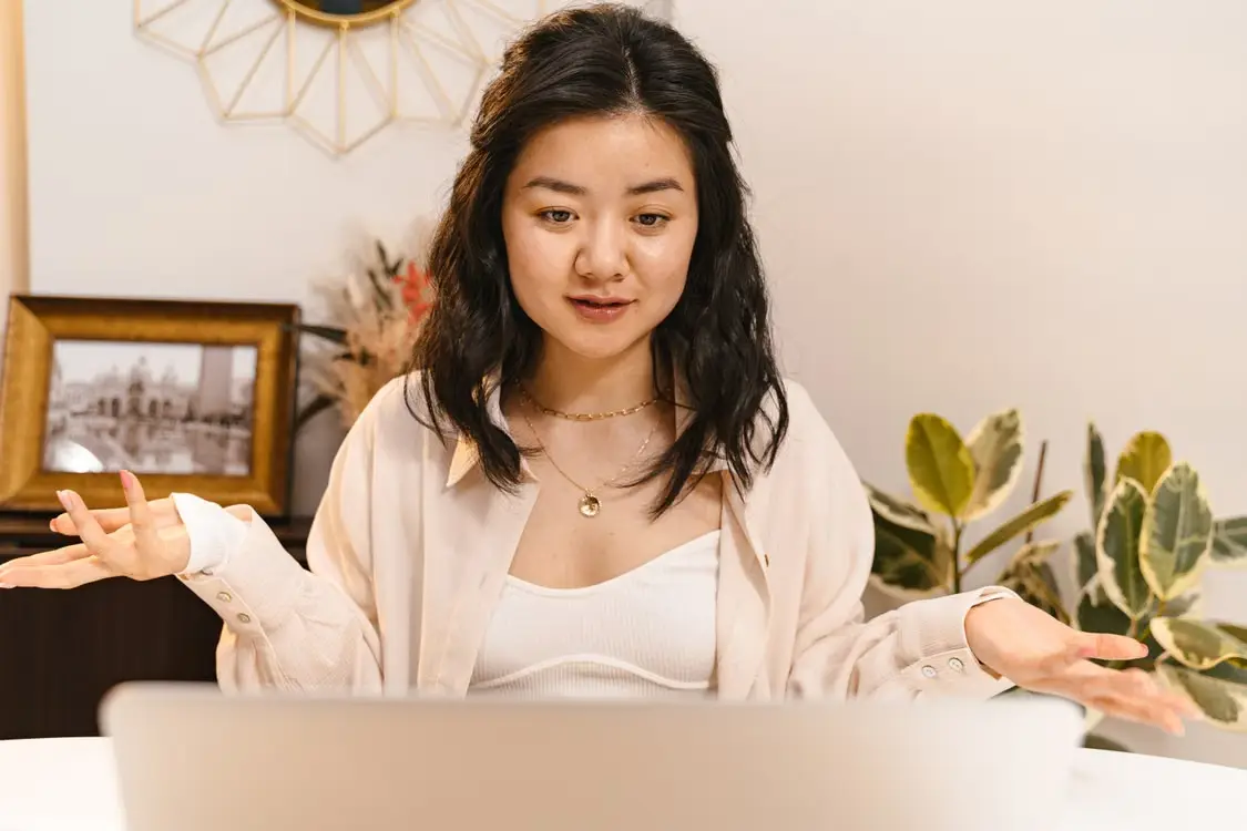 Woman gesturing during an online video call in a home office with plants and framed photos