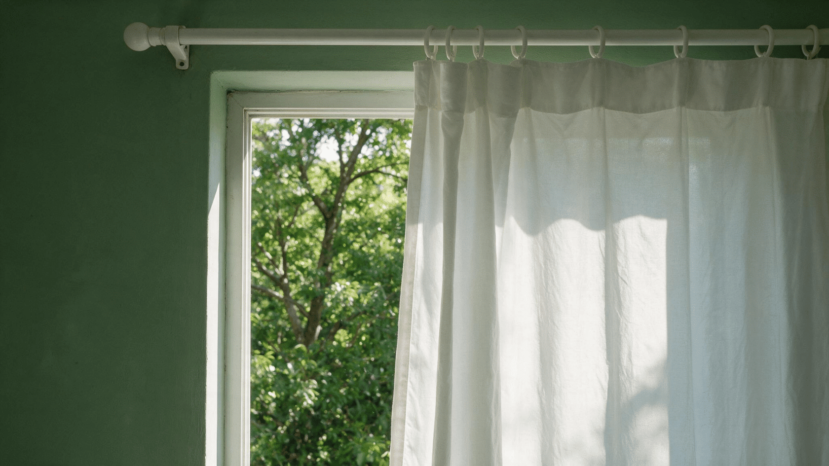 White curtain hung using a tension rod inside the window frame with natural light filtering through.
