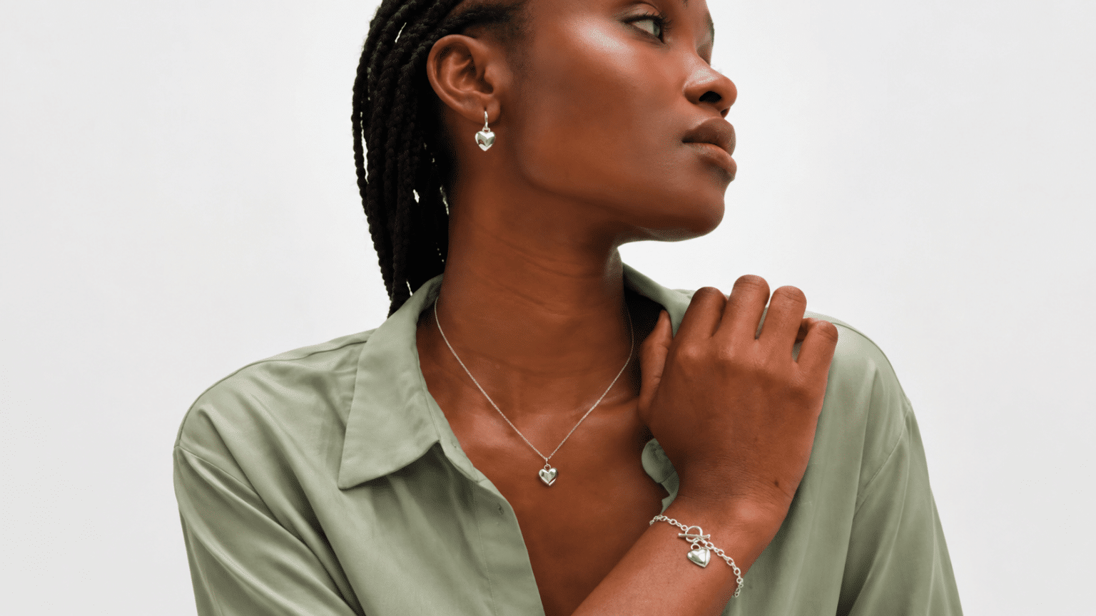 Woman wearing sterling silver heart necklace, earrings, and bracelet with a sage green shirt.