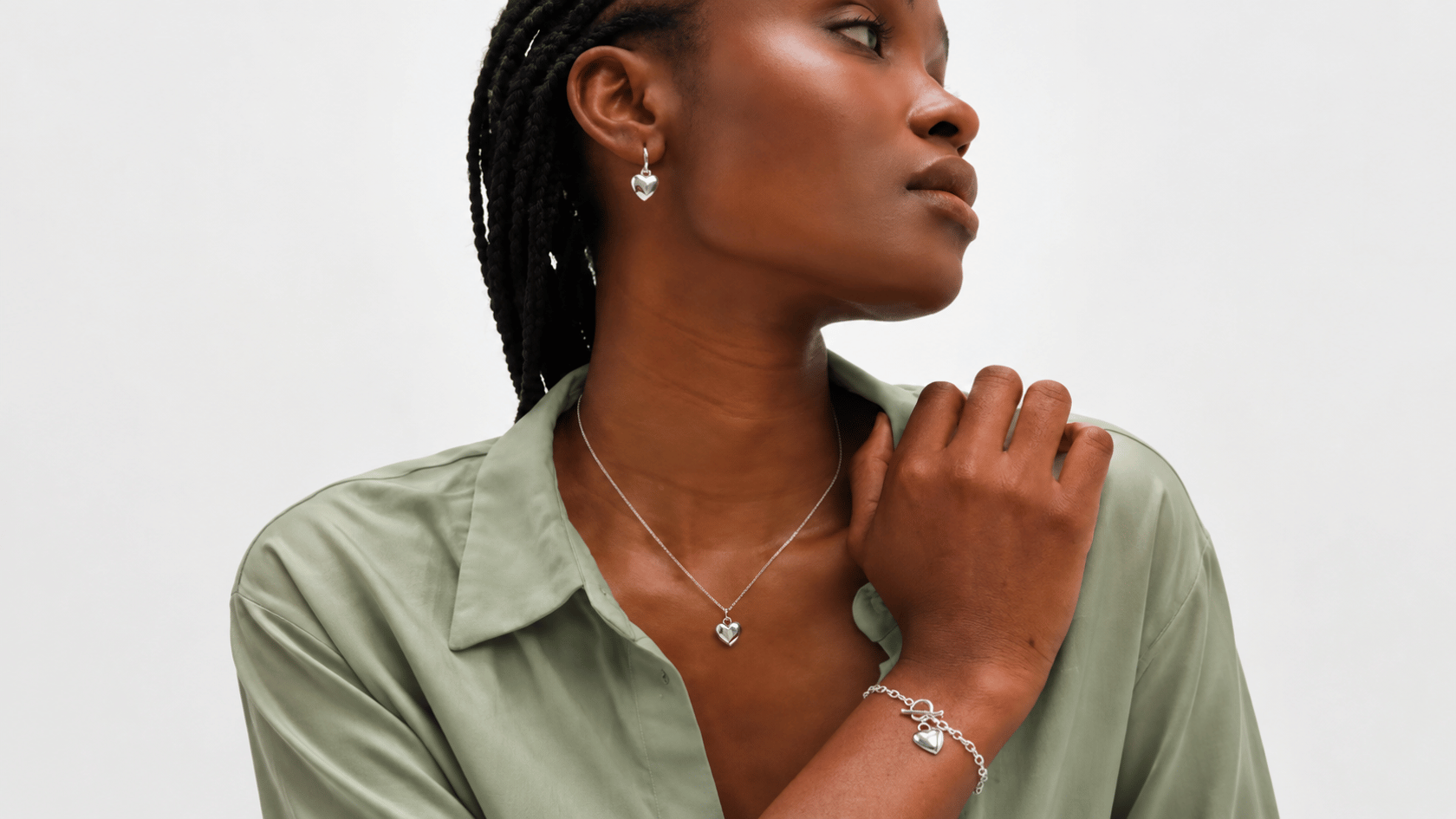 Woman wearing sterling silver heart necklace, earrings, and bracelet with a sage green shirt.