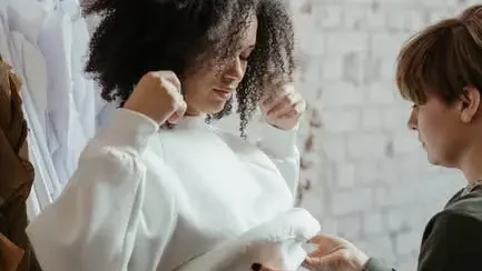 Fashion designer adjusting white sweatshirt on model in studio with brick wall background