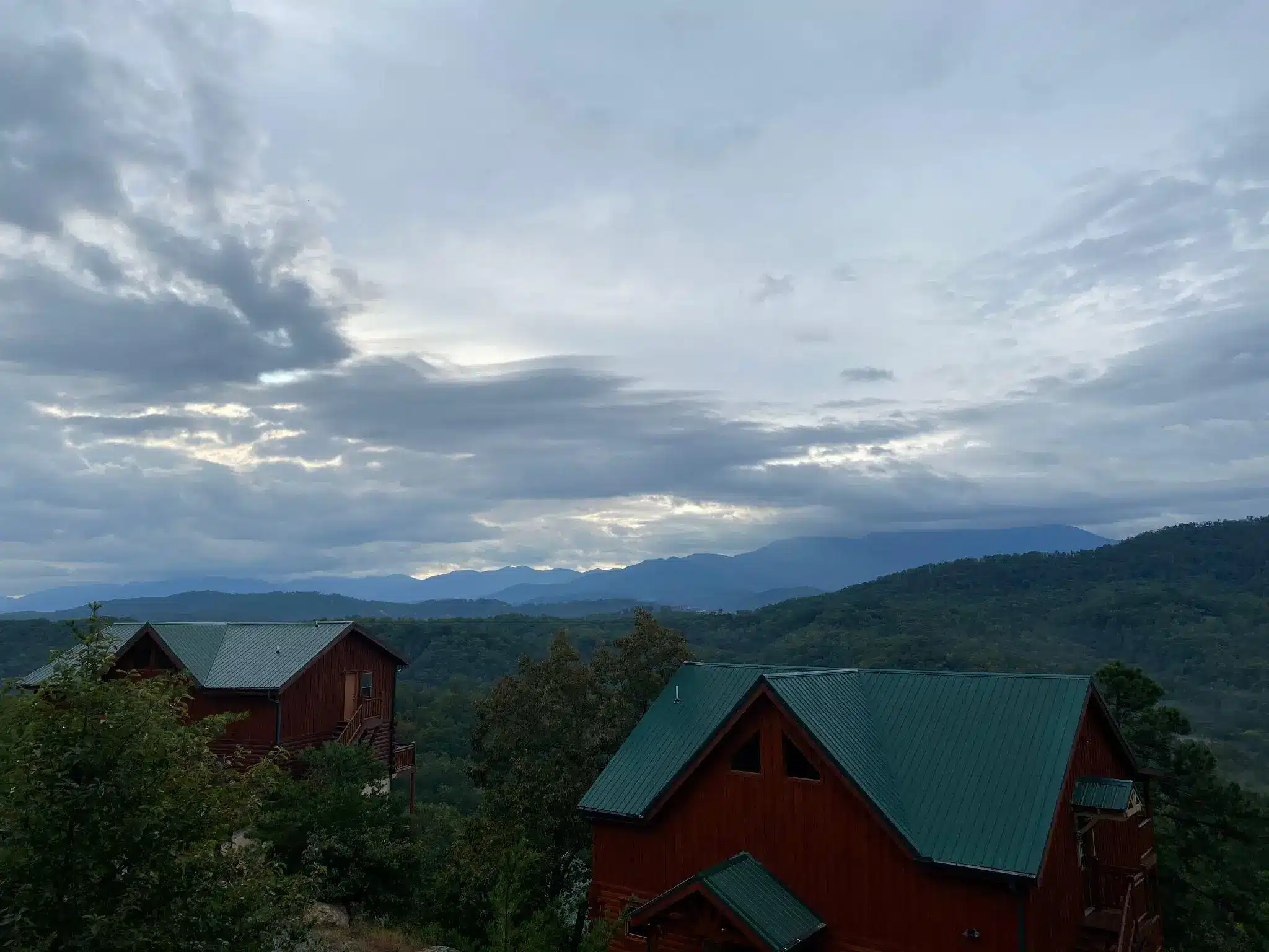Cabins with green roofs nestled in lush mountain landscape under cloudy sky