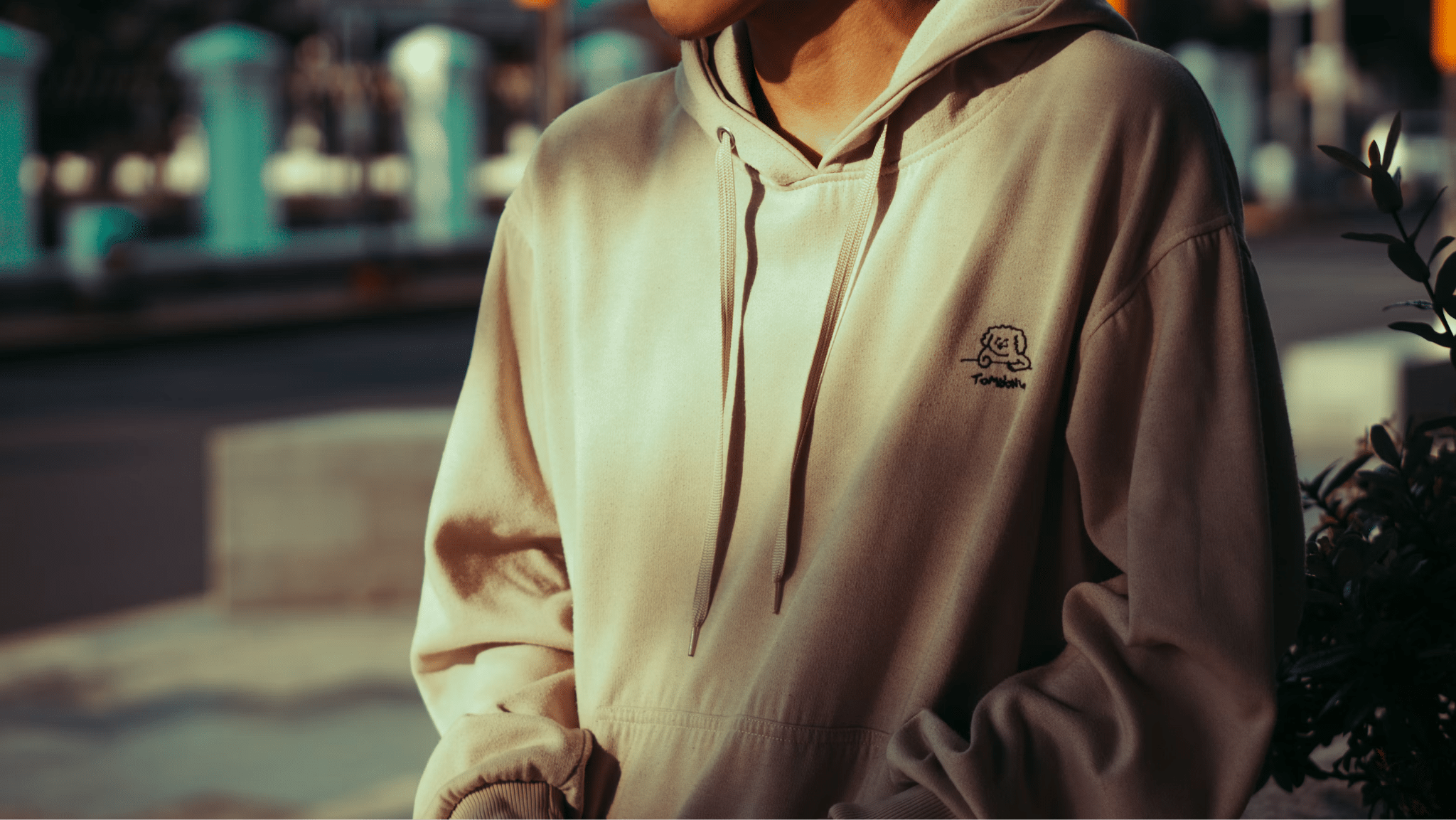 Person wearing beige hoodie outside in urban setting with soft, diffused sunlight