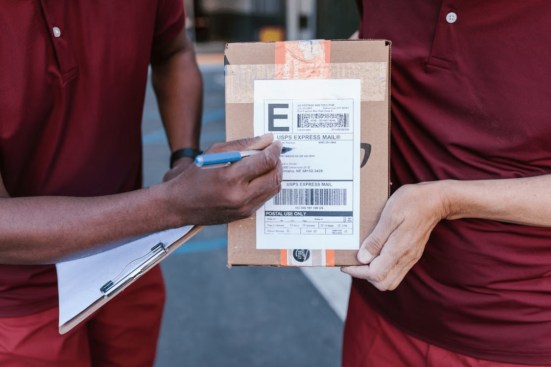 Delivery person signing form on clipboard while holding a labeled package outdoors