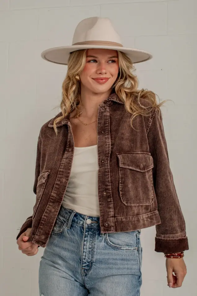 Blonde woman in corduroy jacket and beige hat indoors against white wall
