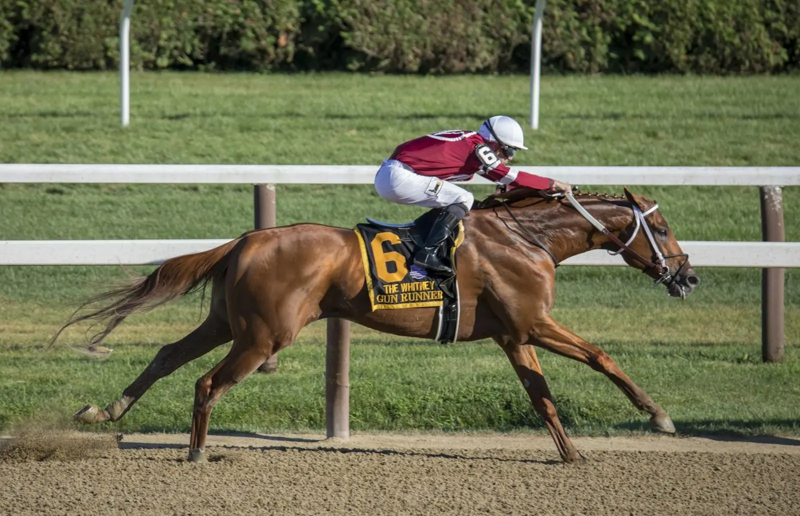 Jockey riding brown racehorse on dirt track during daytime event