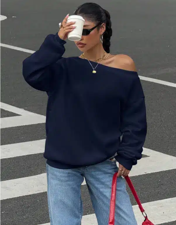Woman in navy sweater holding coffee cup outdoors on a crosswalk, wearing sunglasses and jeans