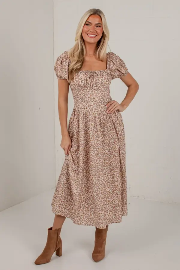 Woman wearing floral print dress and brown ankle boots in plain indoor setting