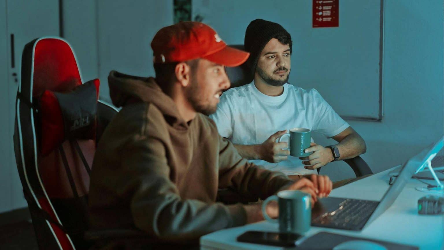 Two men at a desk working on laptops in dimly lit room