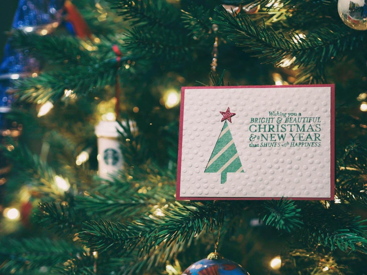 Christmas card with tree design hanging on decorated Christmas tree with ornaments and lights