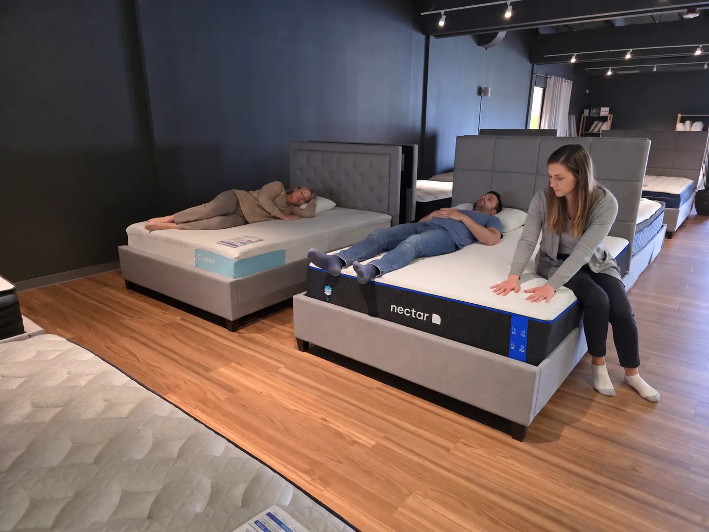 People testing mattresses in a showroom with wooden flooring and modern lighting